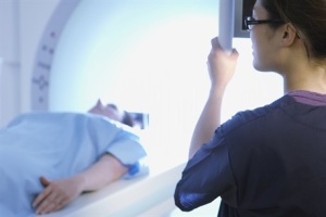 Person on a table going into an MRI scanner while technologist watches